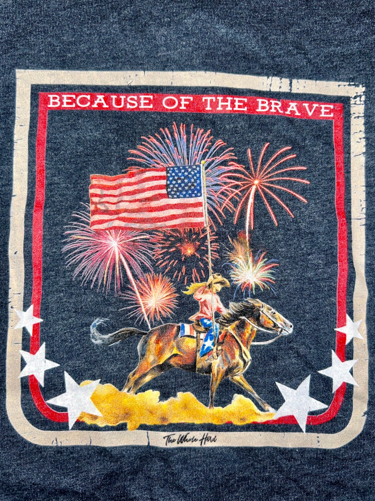 Western Toddler or Youth T-Shirt in the cover navy blue, displaying a cowgirl on her horse holding the American Flag, and the words 'Because of the Brave'