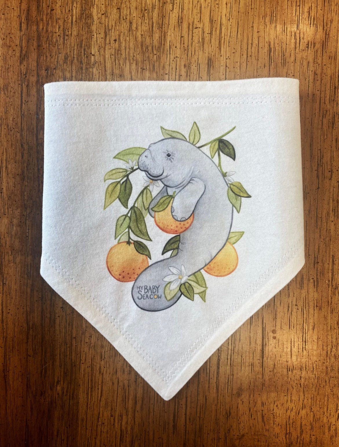 Bandana Style Bib with a manatee hugging an orange, with the words 'My Baby Seacow' 