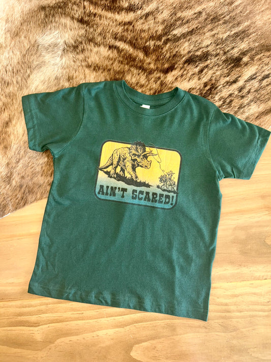 A Unisex fit t-shirt for toddlers and youth. A depiction of a cowboy roping a dinosaur on the front with the words 'Ain't Scared!'. 